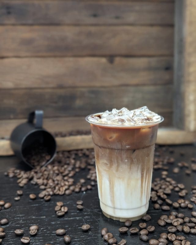 an iced coffee on a table surrounded by coffee beans