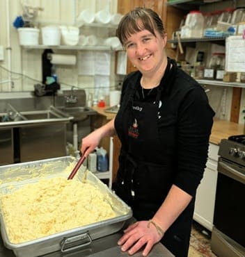 Bakery staff member mixing a large batch of dough or batter in a commercial kitchen prep area.